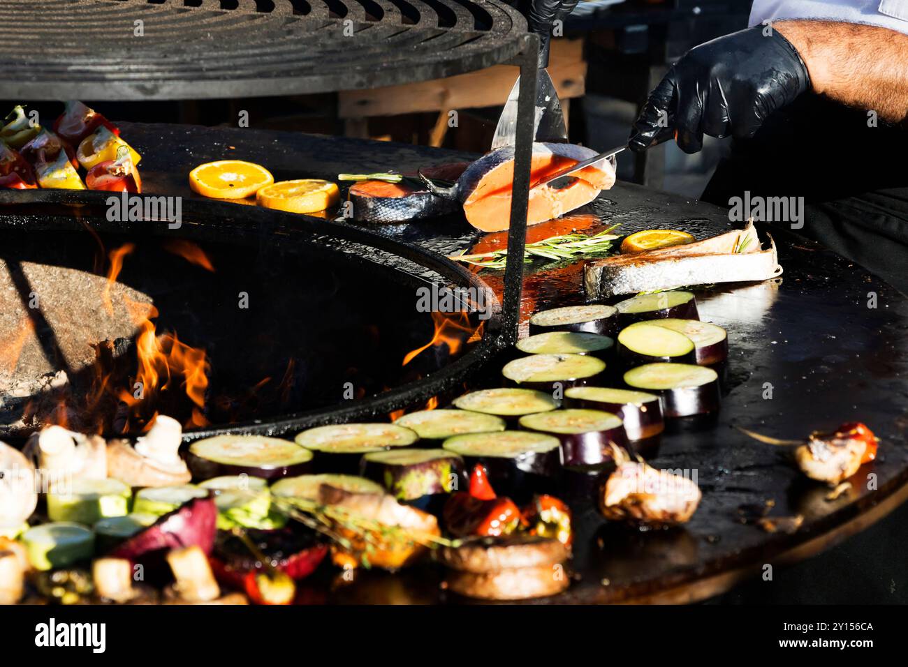 A person who is wearing black gloves is skillfully cooking various types of food on a grill in a wellequipped outdoor kitchen setting Stock Photo