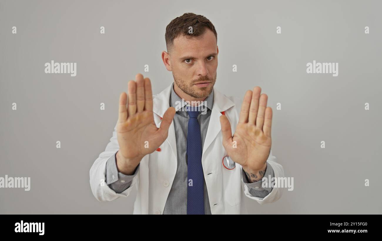 Serious young man in lab coat and tie making stop gesture with both ...