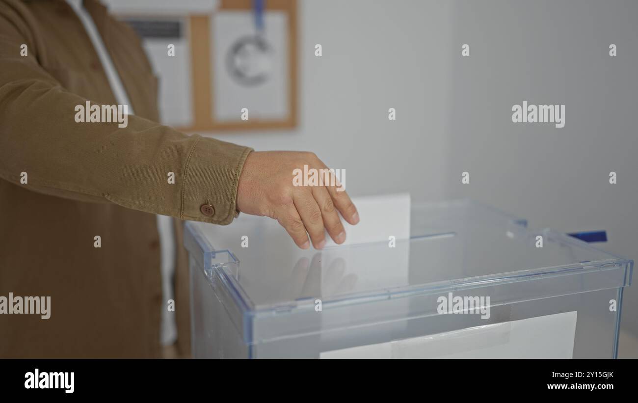 Hispanic man casting vote in ballot box at indoor electoral college. Stock Photo