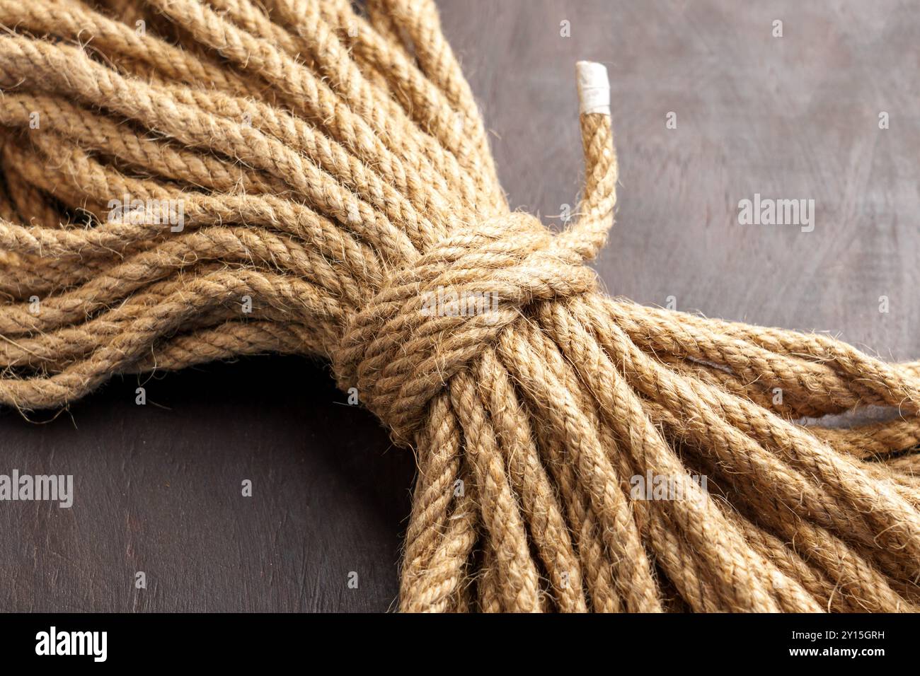 Knotted bundle of rough jute rope on brown board in close up. Stock Photo