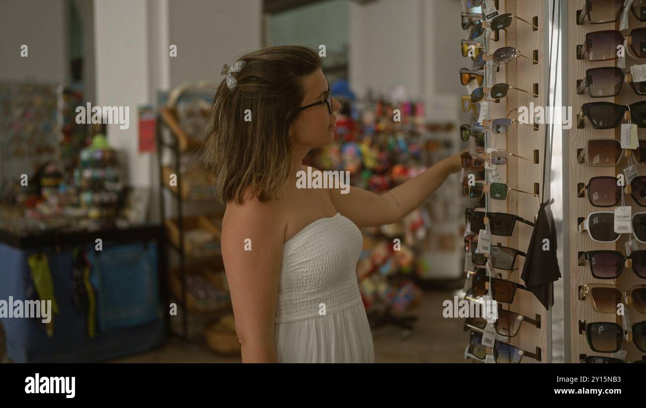 A young hispanic woman shops for sunglasses on a charming street in gallipoli, puglia, italy, surrounded by colorful displays and accessories. Stock Photo