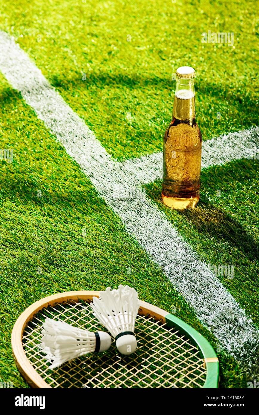 Badminton racket and shuttlecocks rest on green turf beside cold beer ...