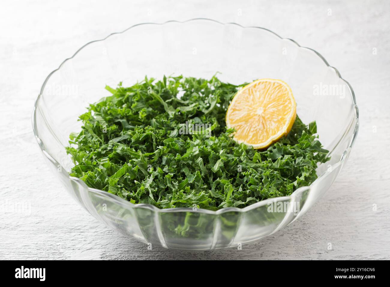 Chopped kale cabbage leaves with lemon in a transparent bowl on a light gray background Stock Photo
