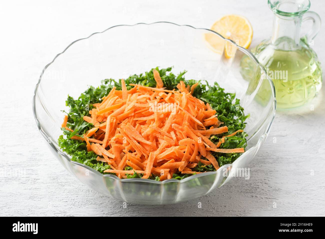 Chopped kale leaves with carrots in a transparent salad bowl on a light gray background Stock Photo