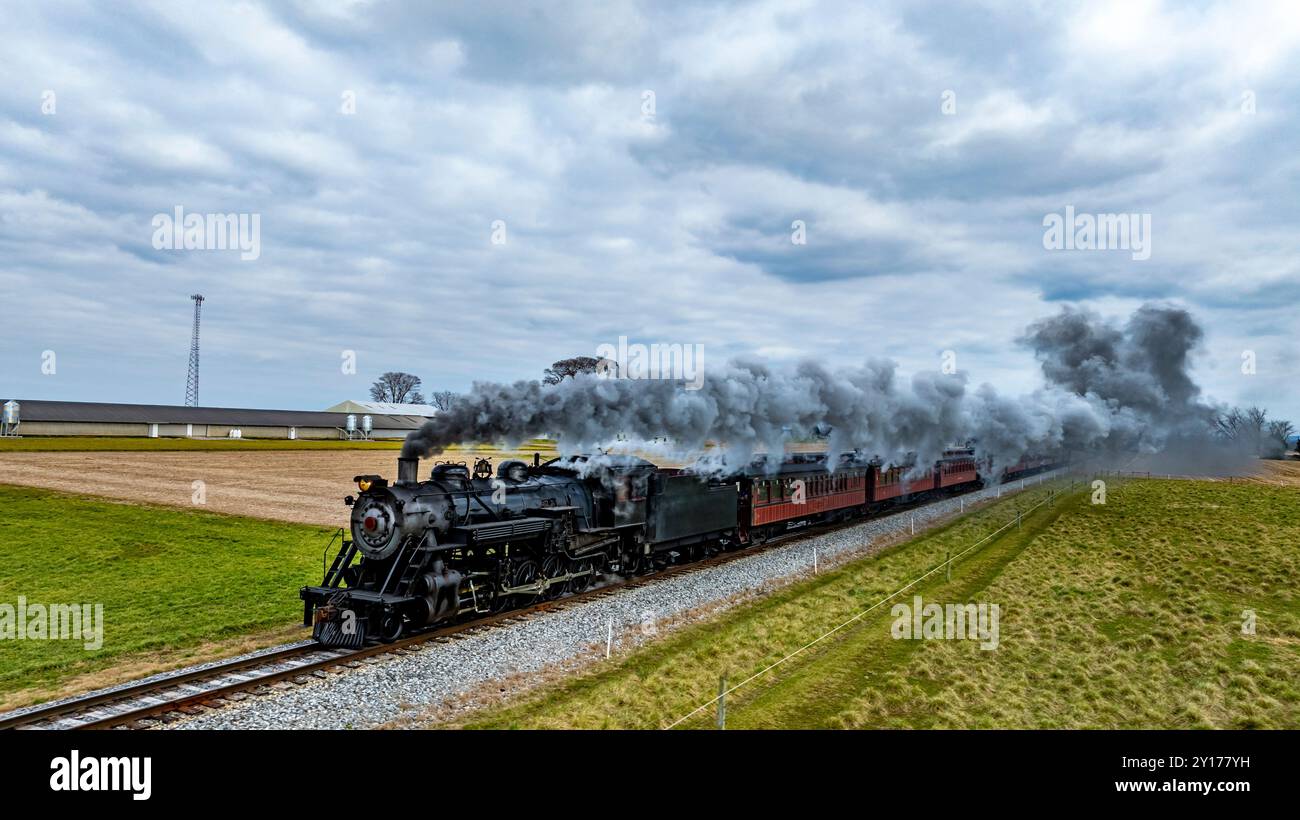 A vintage steam locomotive chugs along a track, releasing clouds of ...