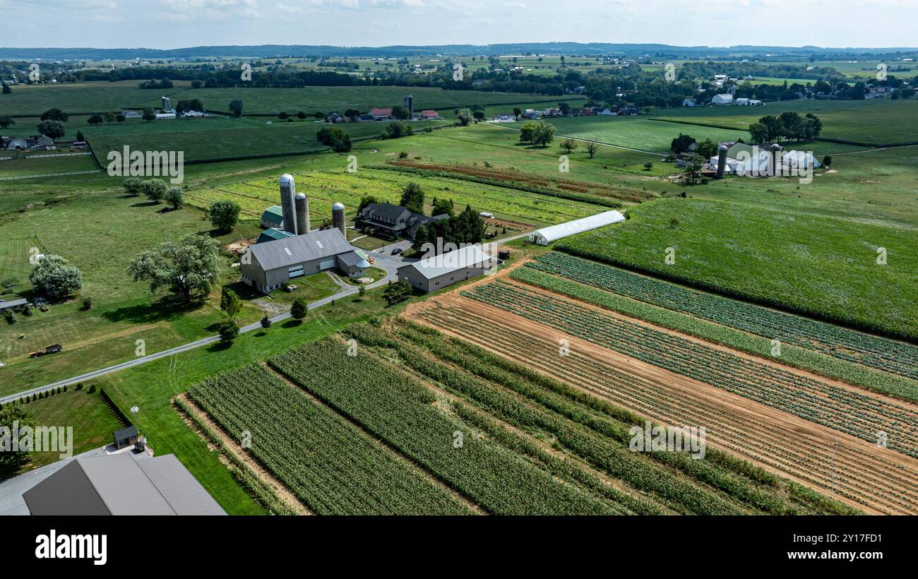 The landscape showcases an expansive rural farm featuring fields, silos ...