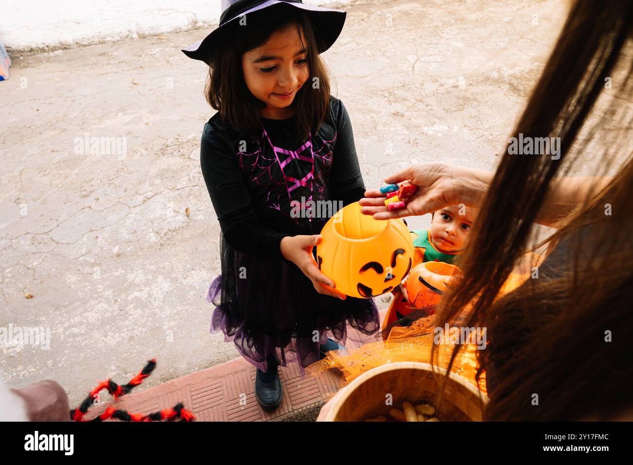 A woman is holding a bowl of candy for a little girl in a Halloween costume. Scene is festive and playful Stock Photo