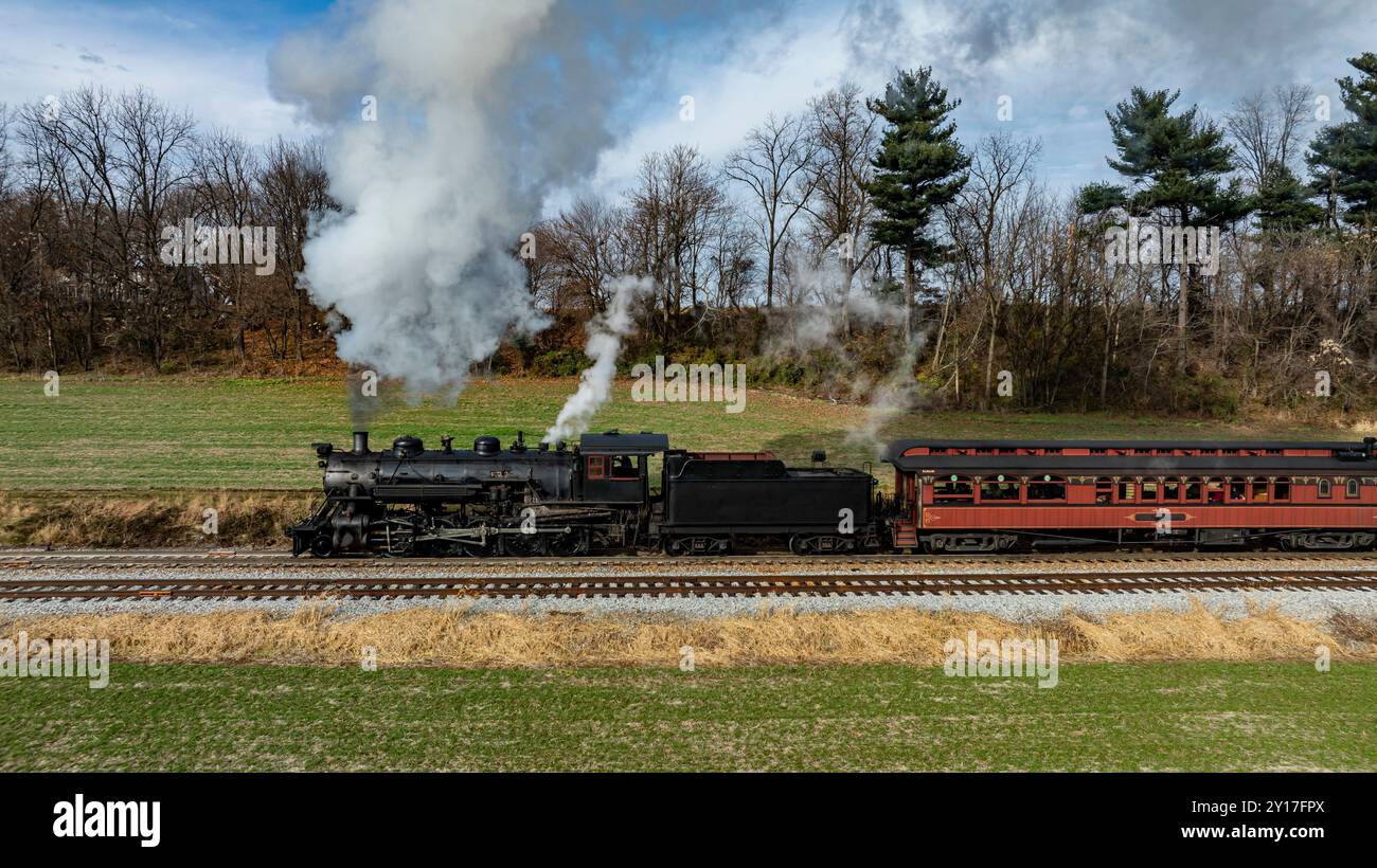 A classic steam locomotive chugs along the tracks, releasing puffs of ...