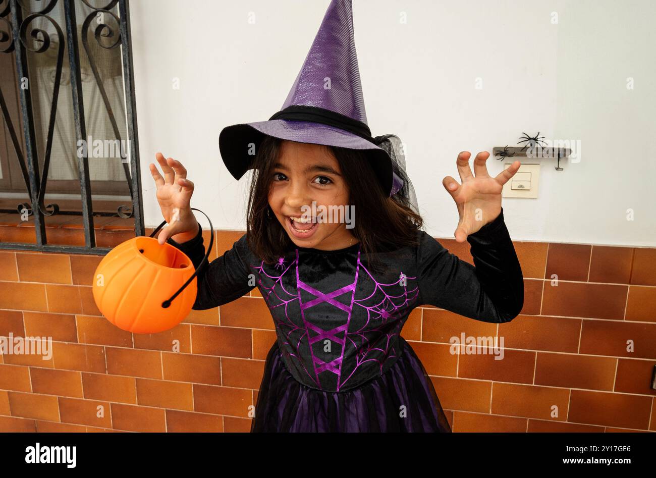 A young girl in a witch costume holding a pumpkin. She is smiling and ...