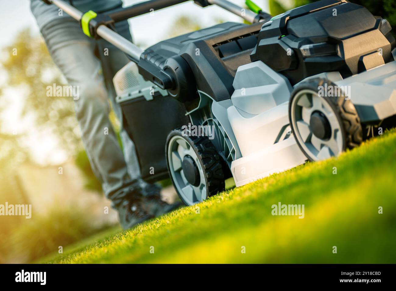 A person is actively mowing a vibrant green lawn on a sunny afternoon, showcasing a neat garden and effective lawn care. Stock Photo