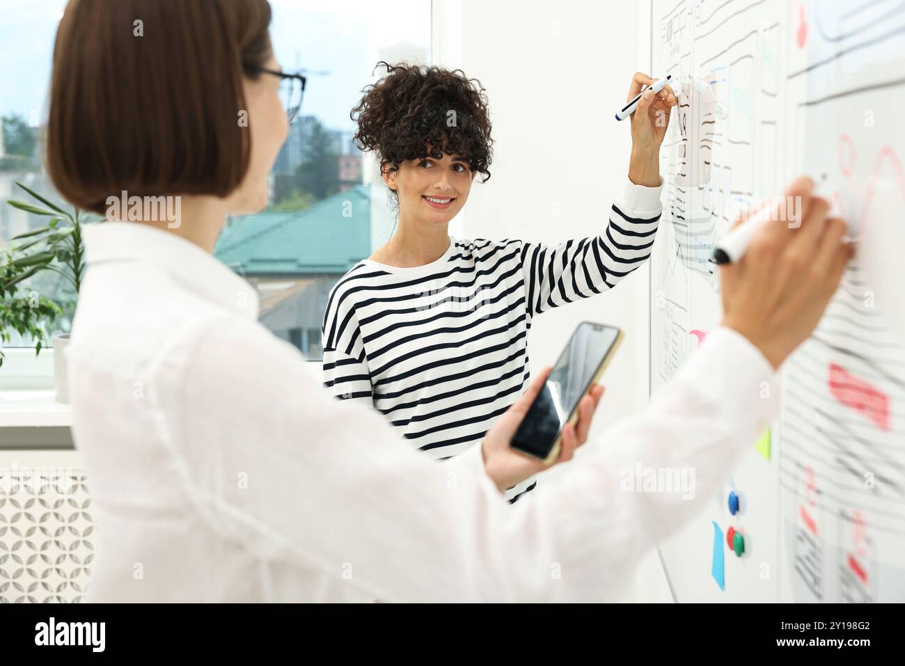 Developing UI design. Women drawing website wireframe on whiteboard indoors Stock Photo