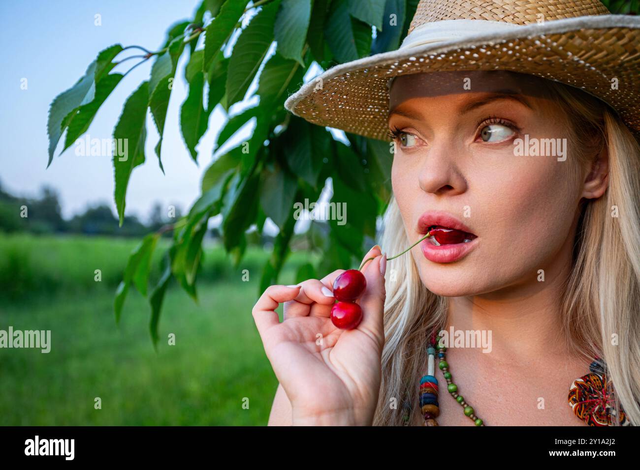 A woman holding a cherry in her mouth, looking sideways Stock Photo