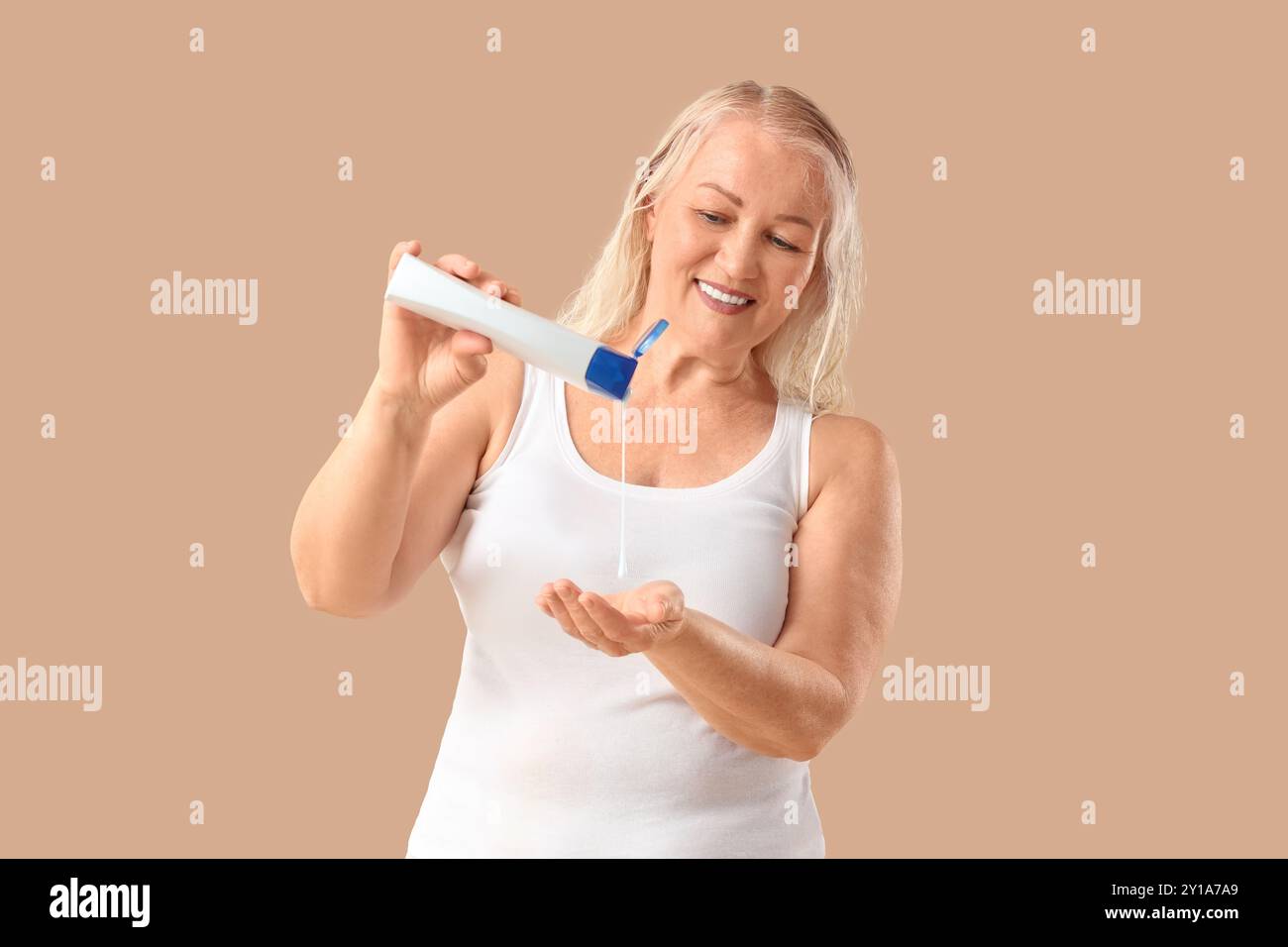 Mature woman pouring shampoo and plant branches on beige background Stock Photo