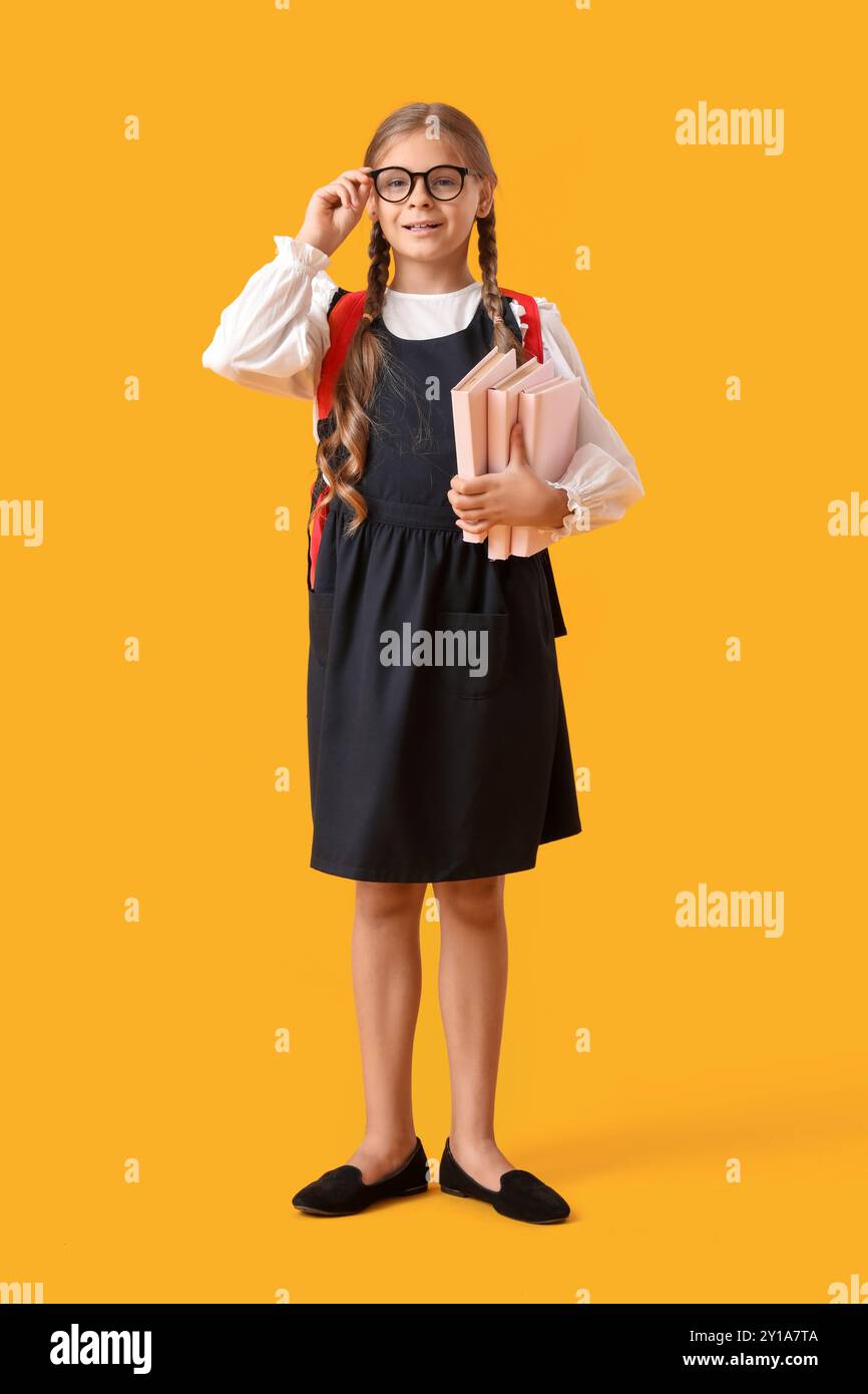 Cute schoolgirl with books and backpack on yellow background Stock ...
