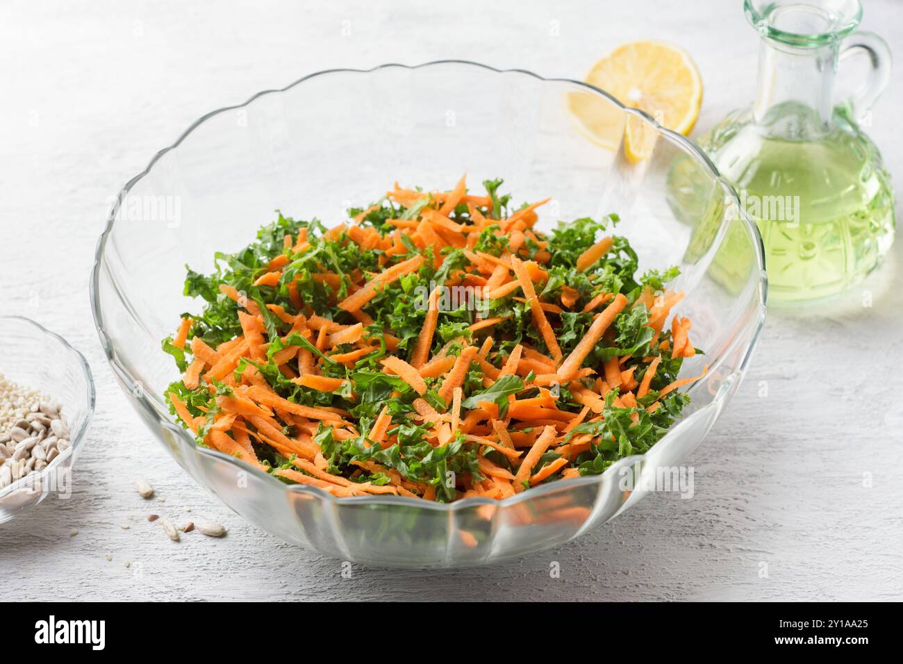 Chopped kale leaves with carrots in a transparent salad bowl on a light gray background Stock Photo