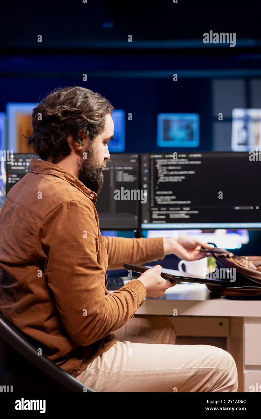 Man packing laptop after finishing doing software quality assurance and reading source code. Developer placing notebook in backpack after inspecting coding on desktop PC and finding all issues Stock Photo