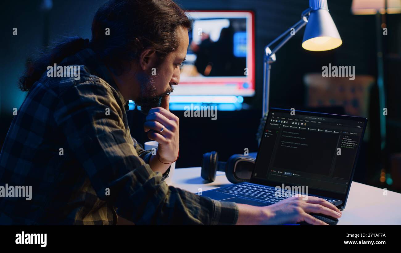 Experienced programmer writes code on laptop screen while in apartment office using Java programming languages. Developer remotely working on fixing database errors while working from home, camera A Stock Photo