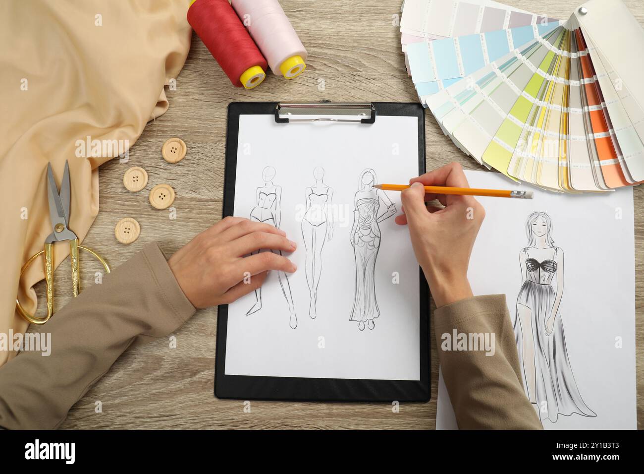 Fashion designer drawing sketch of stylish clothes at wooden table, top ...