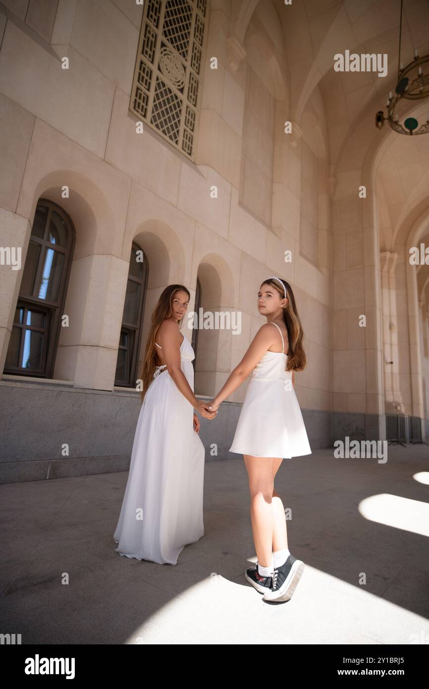 Two women in white dresses stand in a stone building, holding hands ...
