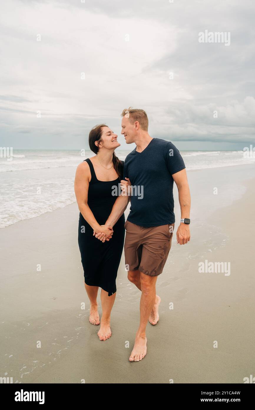 Couple walking hand in hand along the beach, smiling and leaning Stock ...