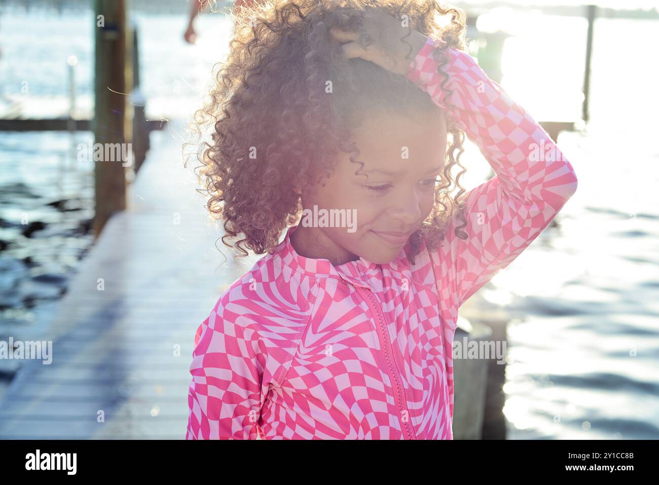 Smiling girl in pink poses by dock, sunlight reflecting on water Stock ...