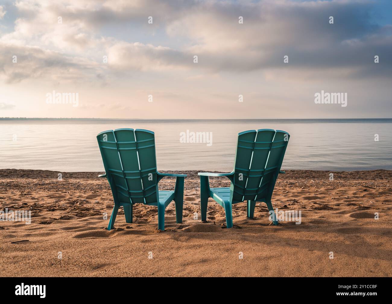 Two teal adirondack chairs on sandy beach with view of lake in summer. Stock Photo