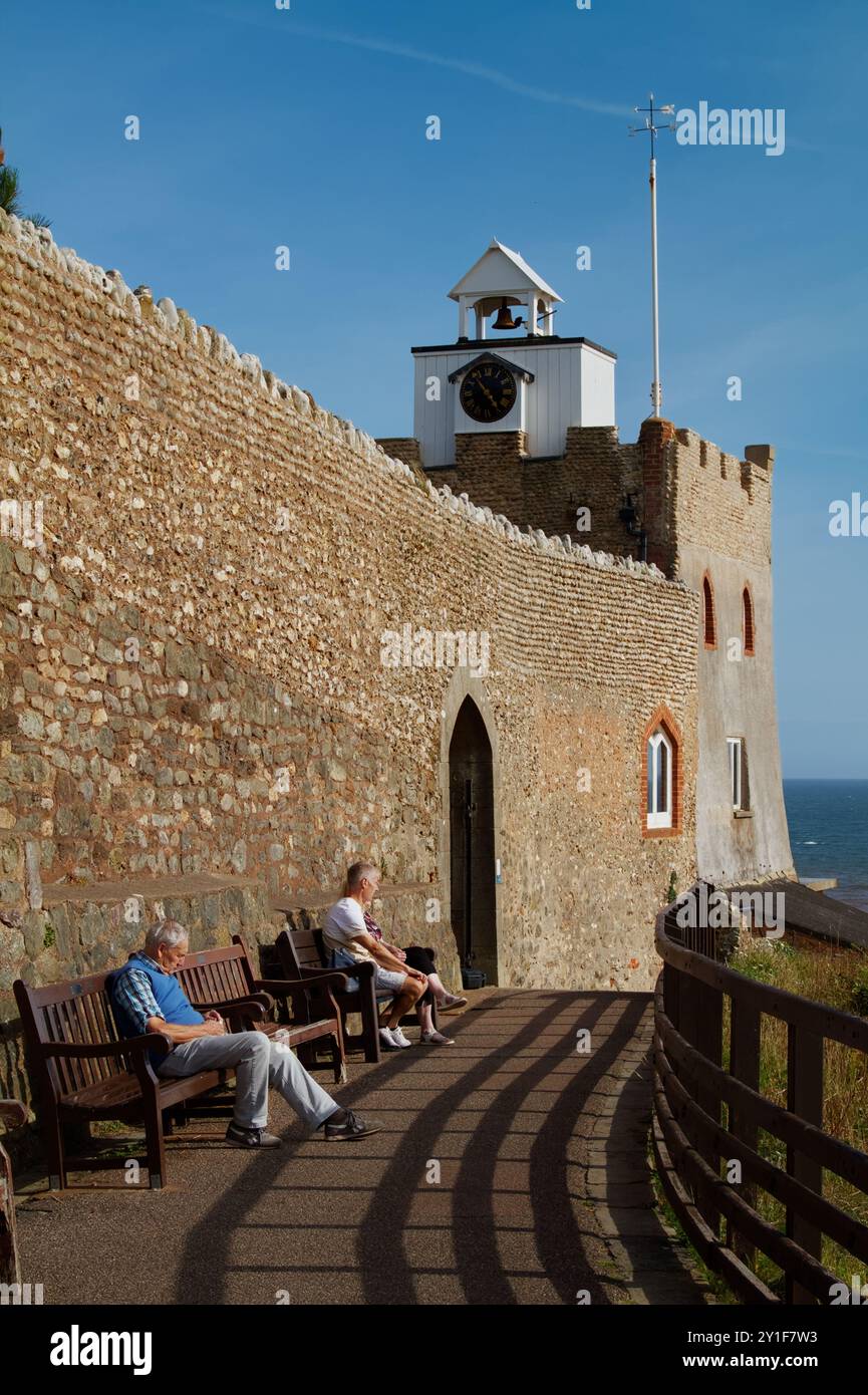 People Sitting On Benches On The Path Underneath The Clock Tower And Flint Wall Of Connaught Gardens, Sidmouth,UK Stock Photo
