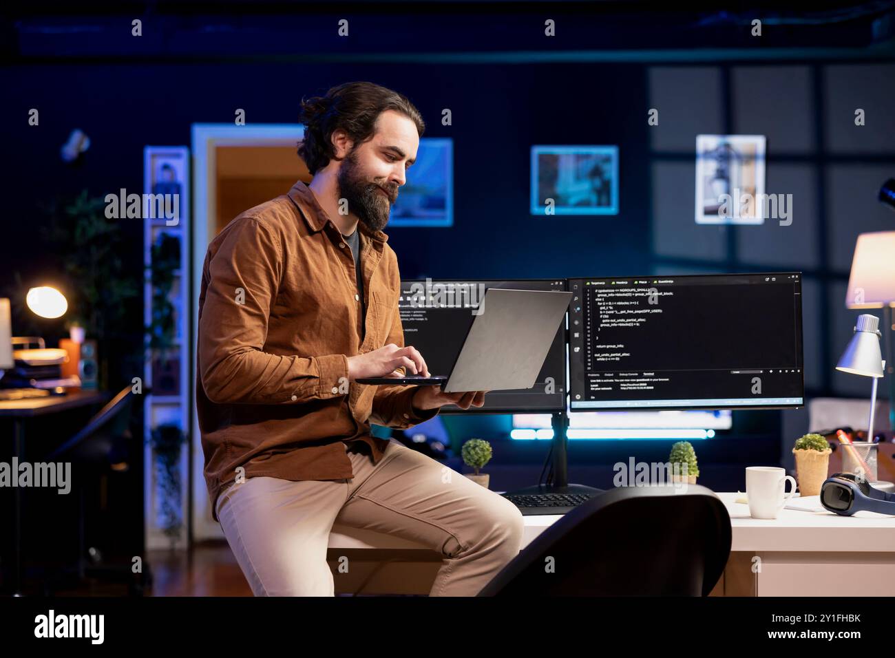 Smiling IT expert doing software quality assurance, reading source code on laptop before implementing it. Happy man sitting on desk inspecting coding on notebook, looking to fix potential issues Stock Photo