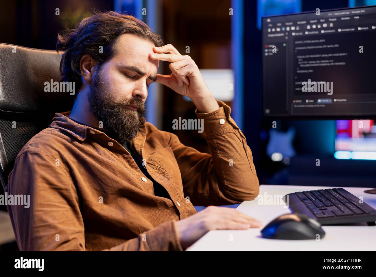 Tired man hurting from too much stress accumulated while doing software quality assurance, reading source code on computer. Developer suffers from headache after inspecting coding on PC for too long Stock Photo
