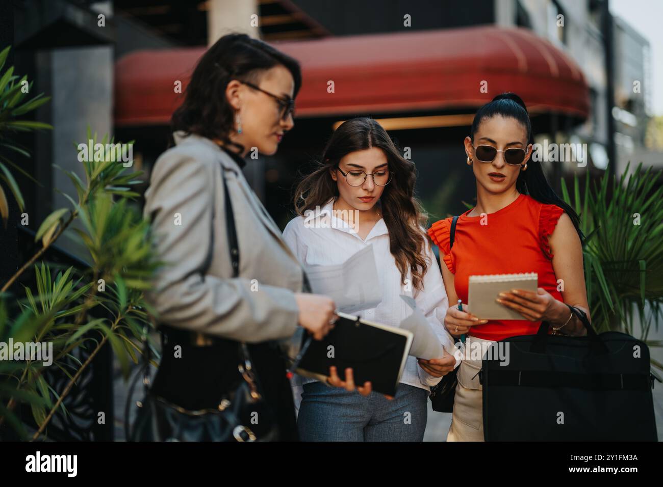 Three businesswomen collaborating outdoors on projects and discussing documents Stock Photo