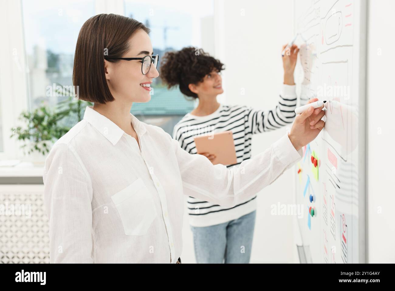 Developing UI design. Women drawing website wireframe on whiteboard indoors Stock Photo