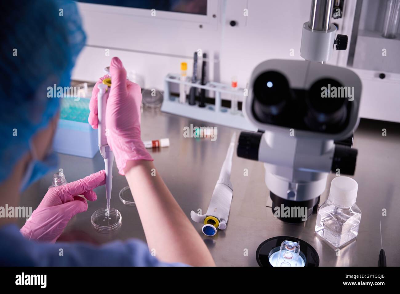 Scientist using a pipette near a microscope Stock Photo