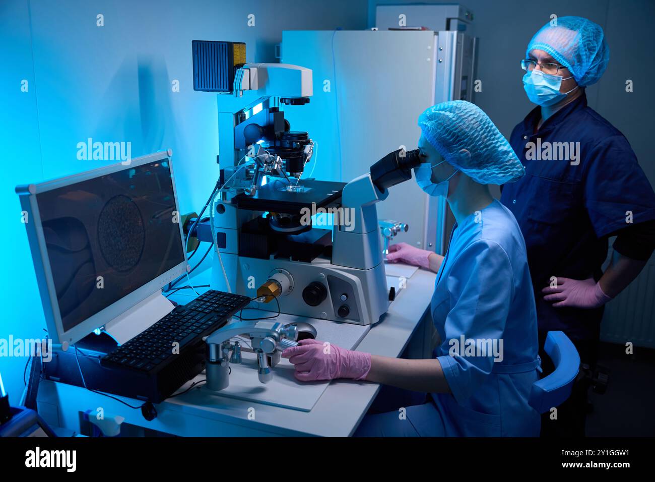 Scientists using a microscope and computer in a sterile laboratory ...