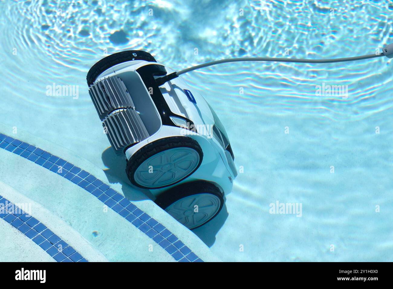 Robotic pool cleaner with a long hose cleaning the bottom of a clear blue swimming pool on a sunny day underwater Stock Photo