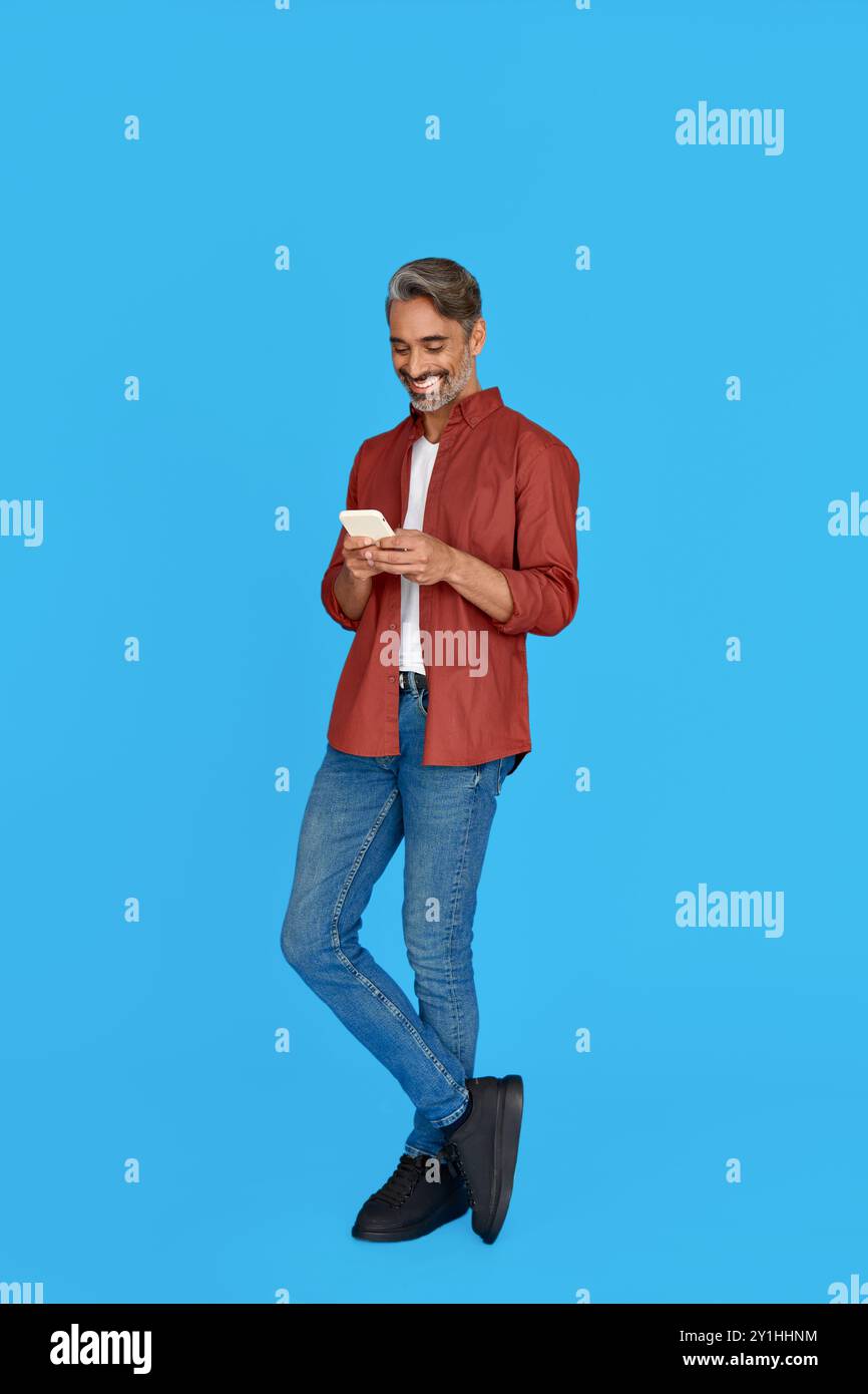 Smiling middle aged man using mobile phone isolated on blue background. Stock Photo