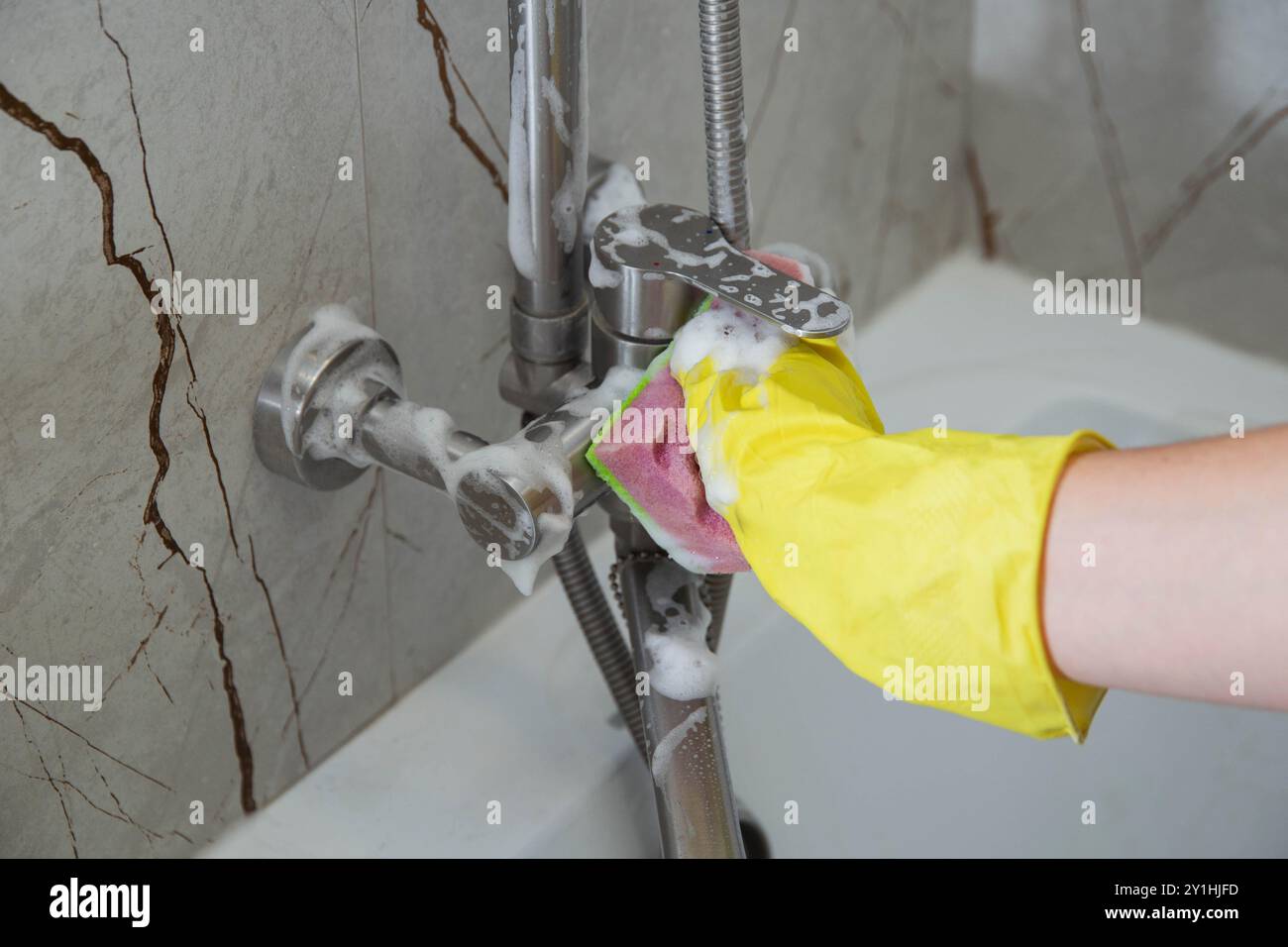 A girl's hand in a yellow rubber glove washes a water tap in the ...