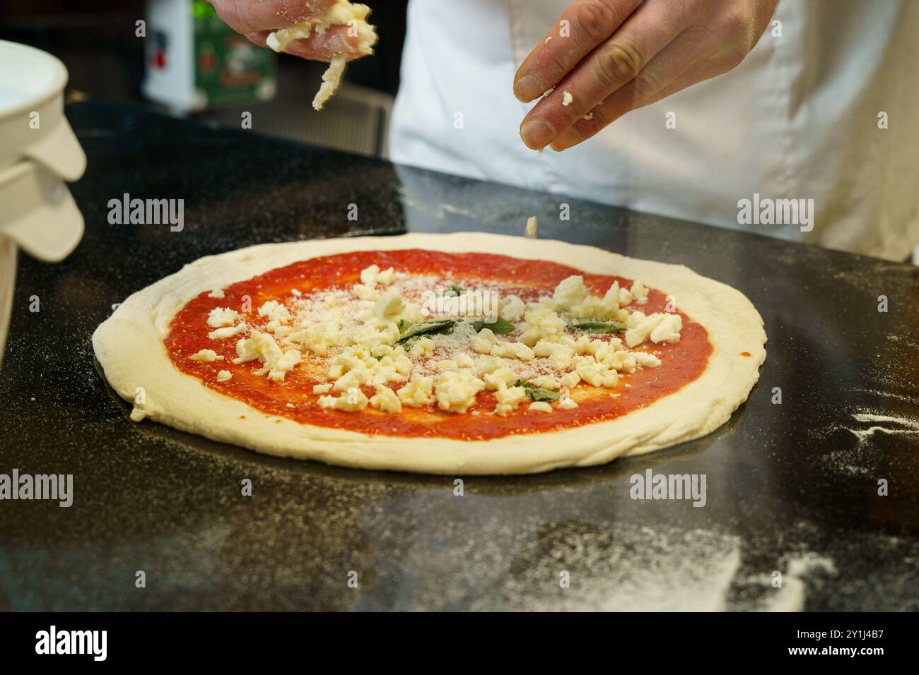A chef preparing a pizza with tomato sauce and spreading mozzarella cheese on pizza Stock Photo