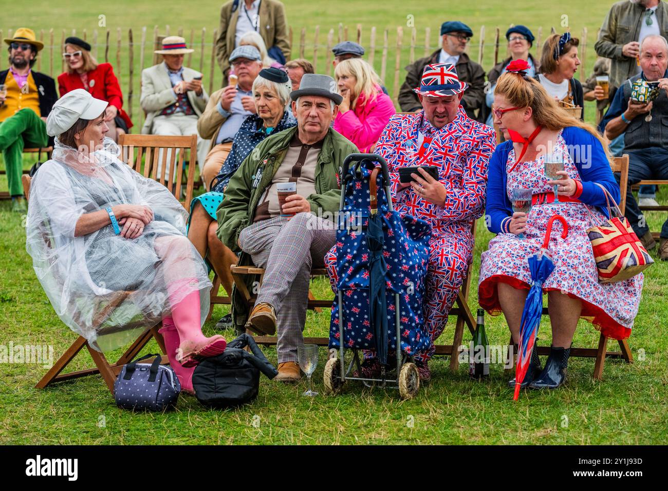 Goodwood, UK. 7th Sep, 2024. People take a breather in patriotic outfits, some with extra protection from the rain, which comes and goes - The Goodwood revival - The only historic motor race meeting to be staged entirely in a period theme, an immersive celebration of iconic cars and fashion. Credit: Guy Bell/Alamy Live News Stock Photo
