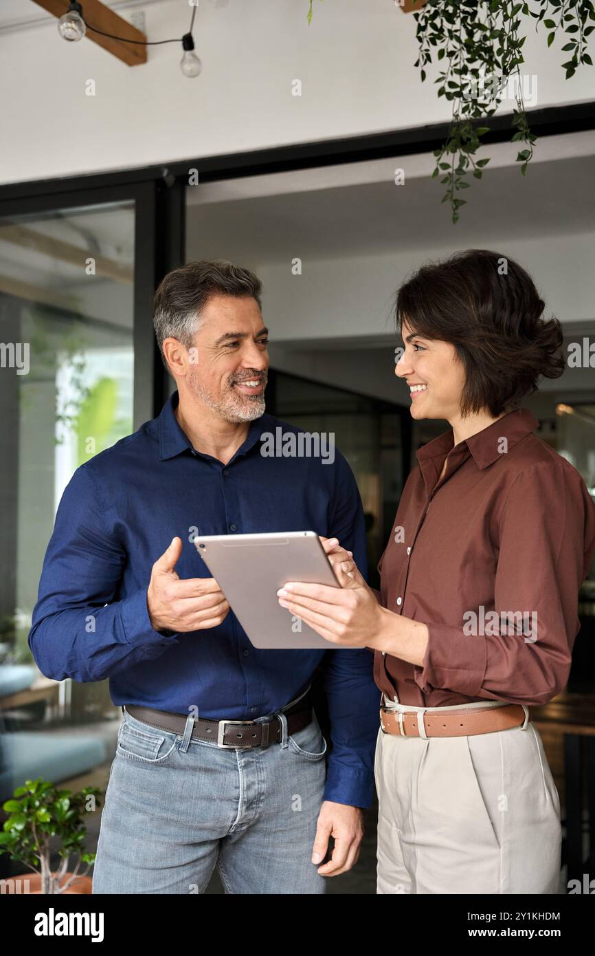 Happy busy company managers using tablet working together standing in office. Stock Photo