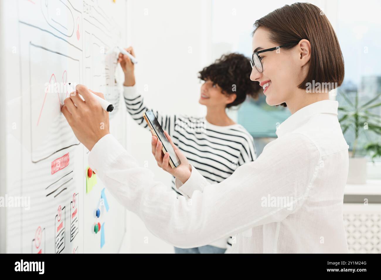 Developing UI design. Women drawing website wireframe on whiteboard indoors Stock Photo