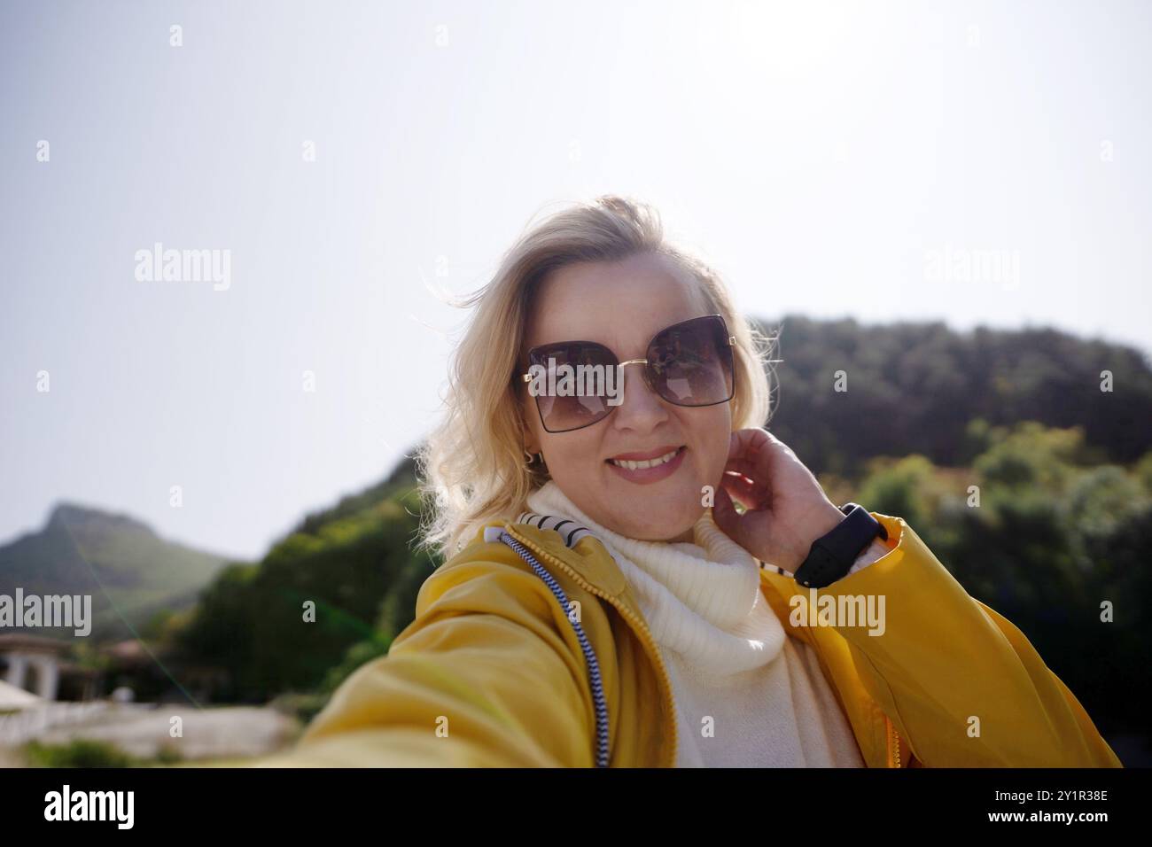 A woman wearing a yellow jacket and sunglasses is smiling for the camera Stock Photo