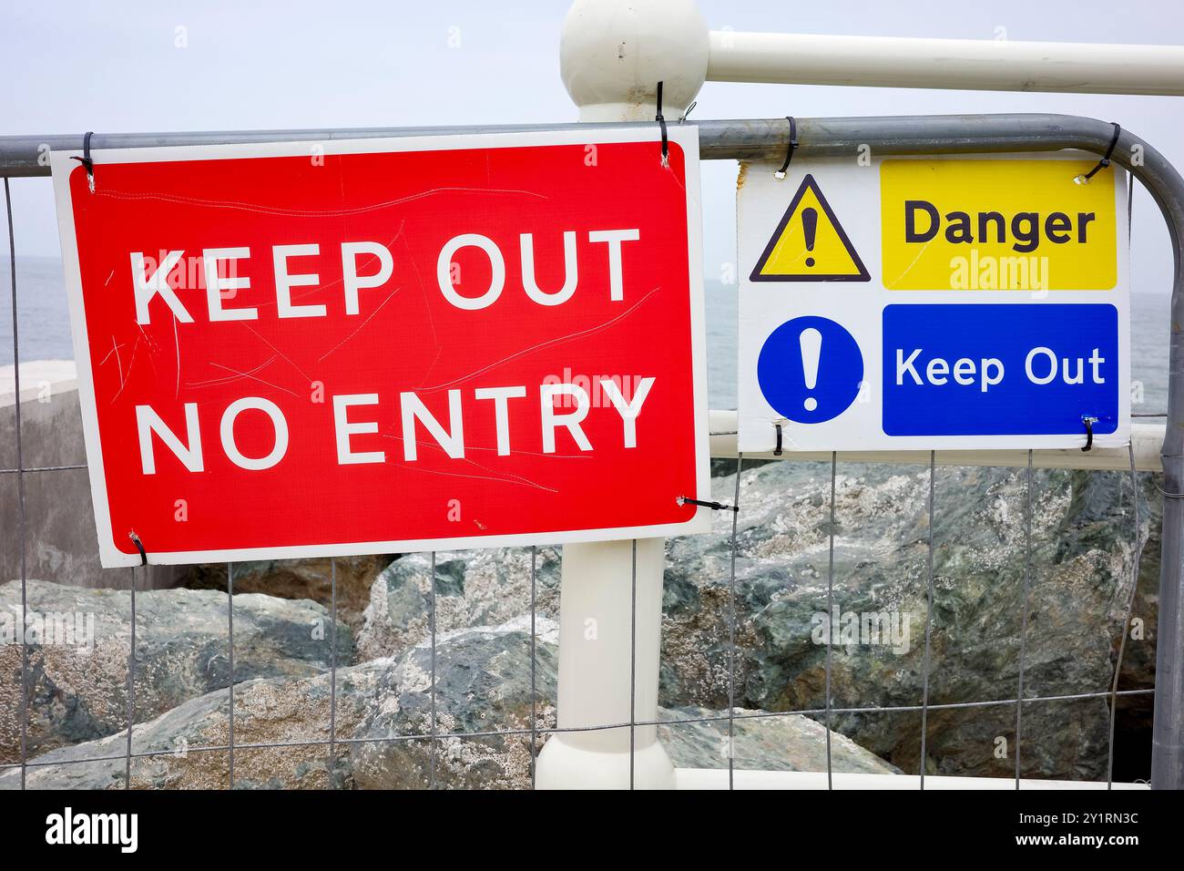 Colwyn Bay, North Wales, UK, 09-08-2024. Red and blue 'Keep Out' signs on a fence by the sea, warning of danger ahead. Stock Photo