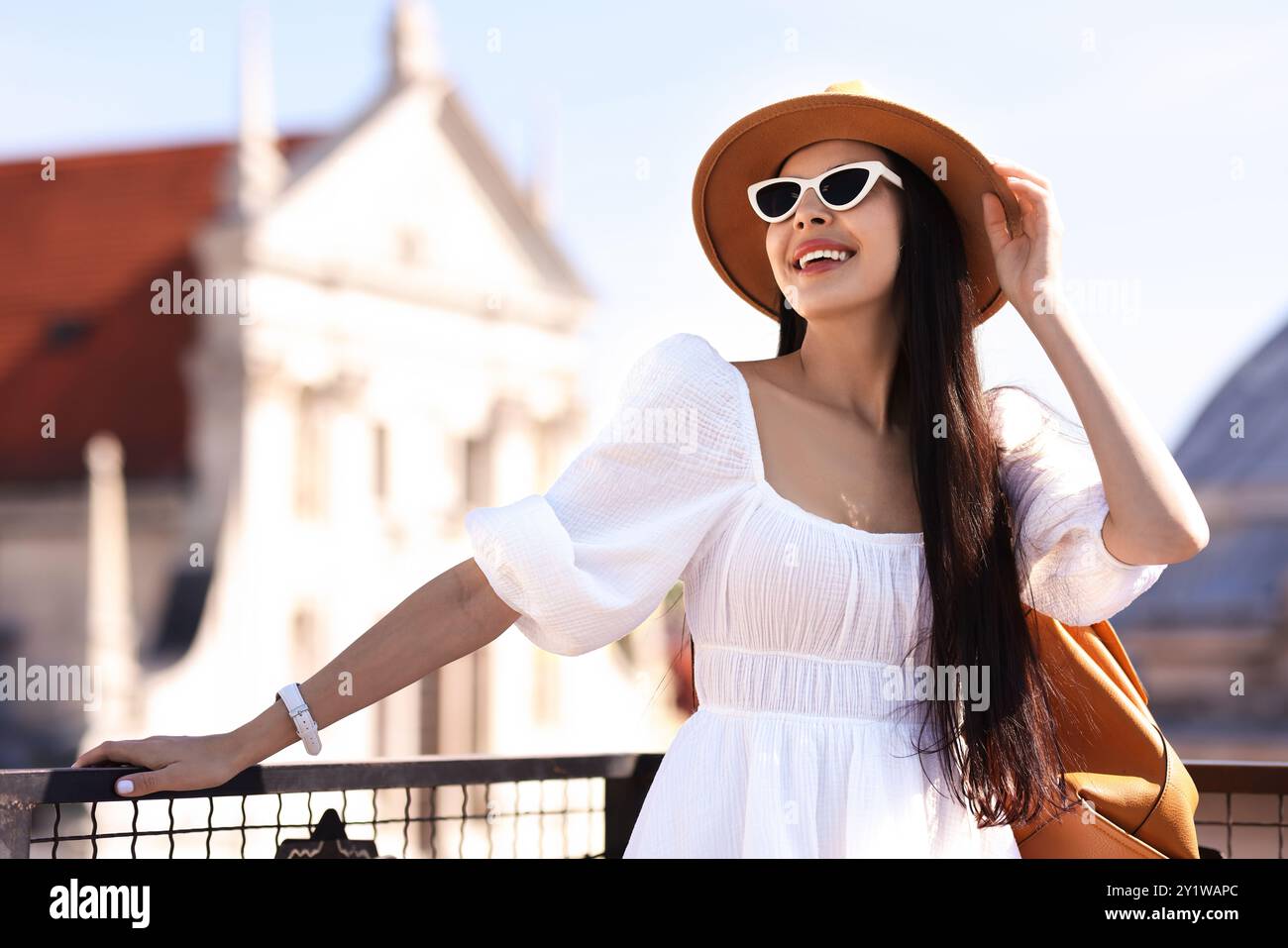 Smiling woman in stylish hat and sunglasses with backpack on city street Stock Photo