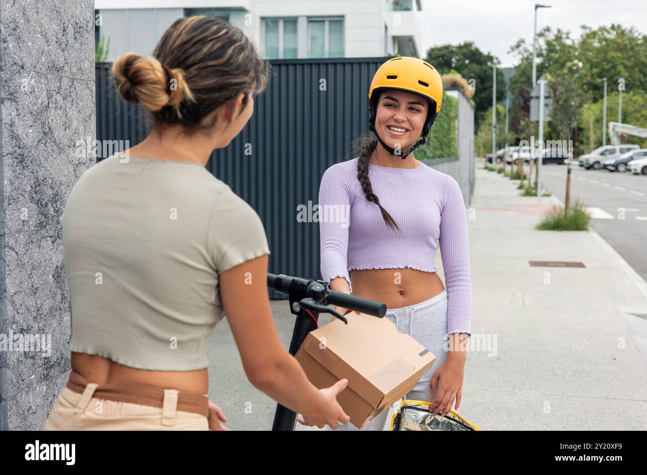 Courier Riding smiling Latin courier, riding an electric scooter, is handing a package ...