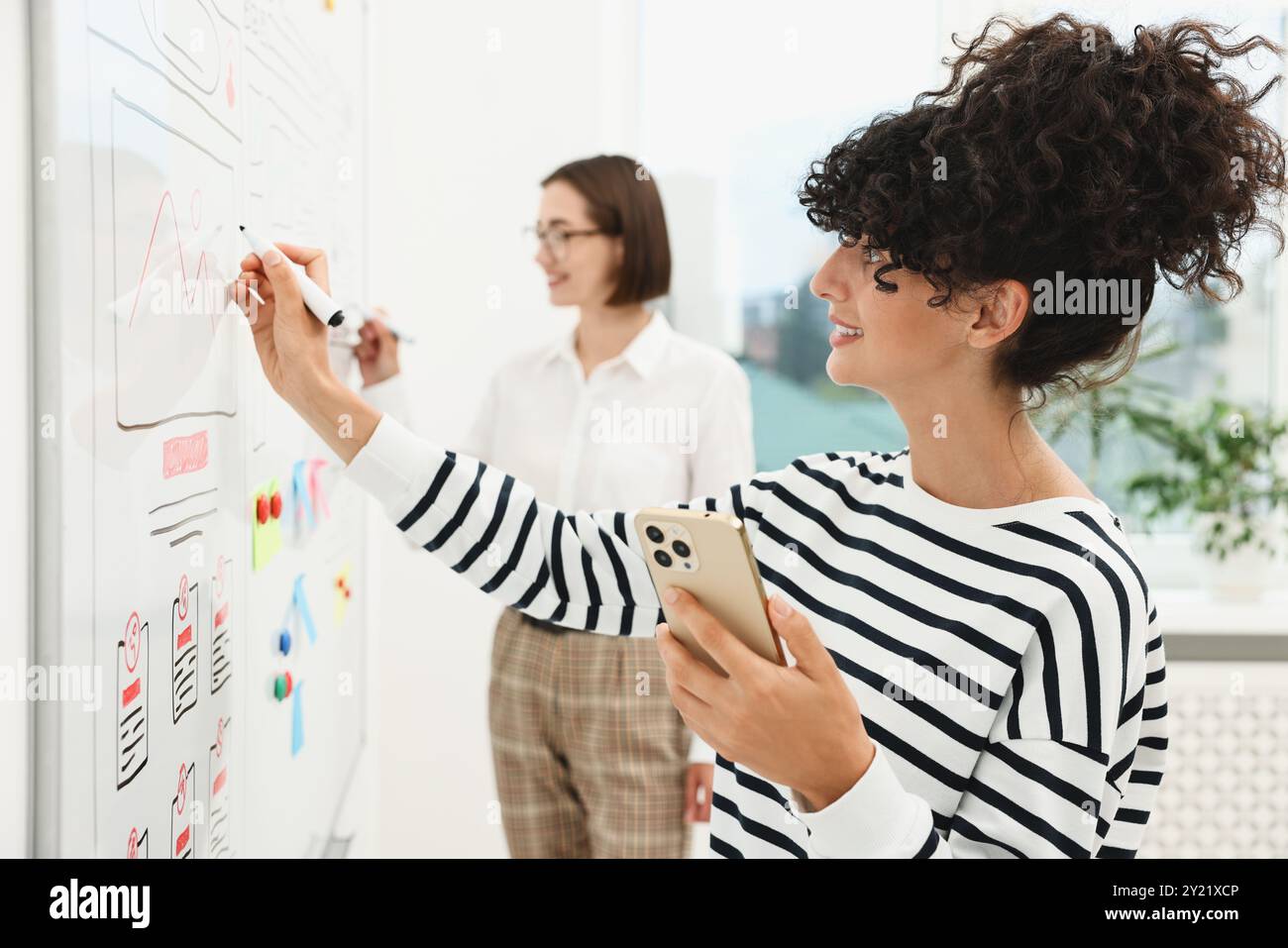 Developing UI design. Women drawing website wireframe on whiteboard indoors Stock Photo