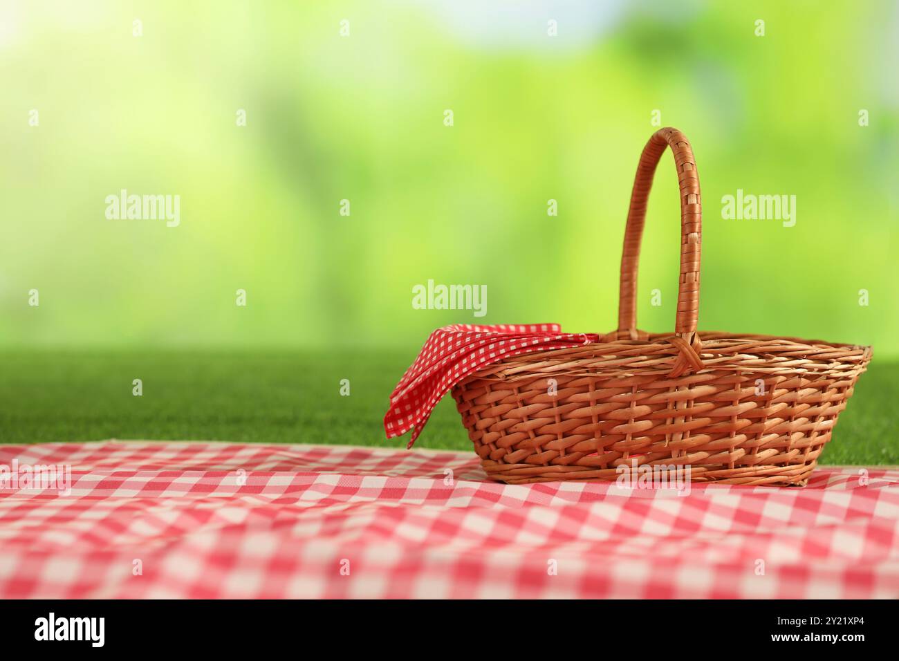 One picnic wicker basket with checkered napkin and blanket on grass ...