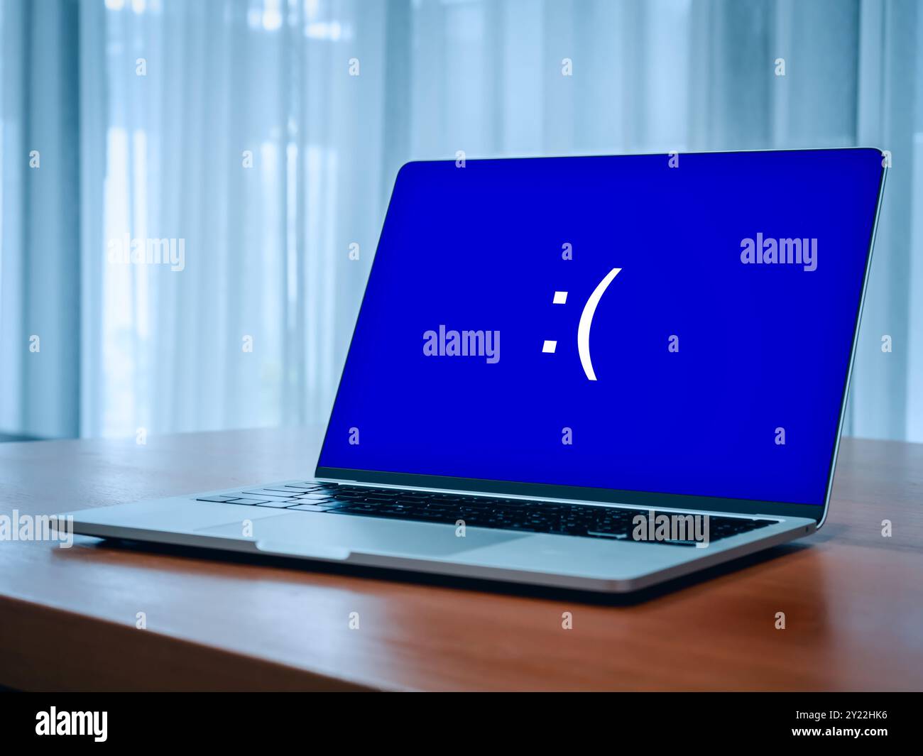 System error concept. Blue screen of death or BSOD showing, big sad emotion face, emoticon on blue display on laptop on table while problem or somethi Stock Photo