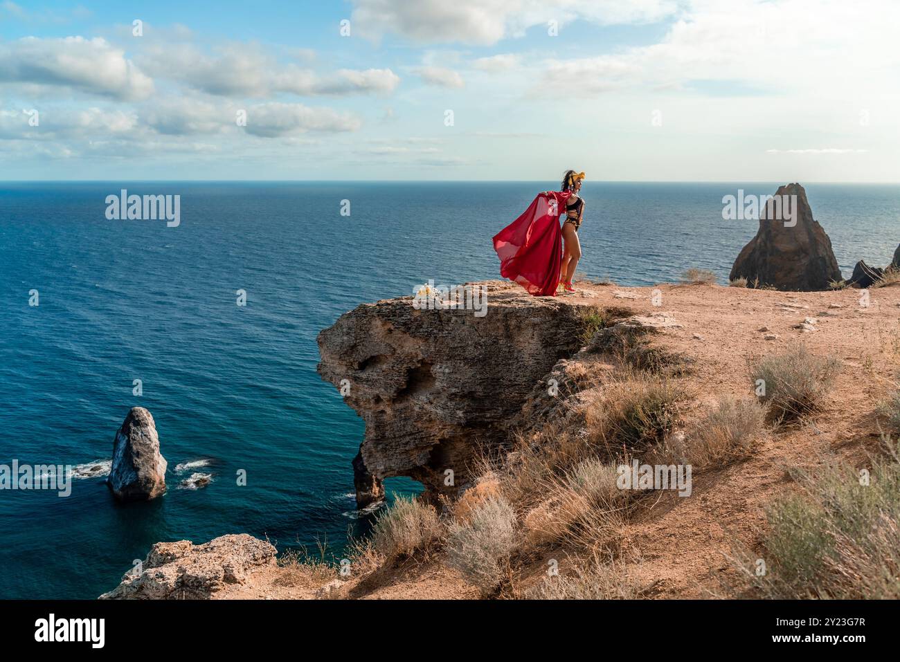 A woman in a red dress is standing on a rocky cliff overlooking the ...