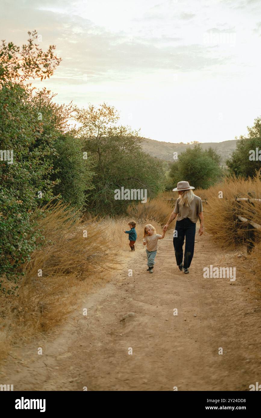 Mom and two children walk down nature trail at sunset Stock Photo