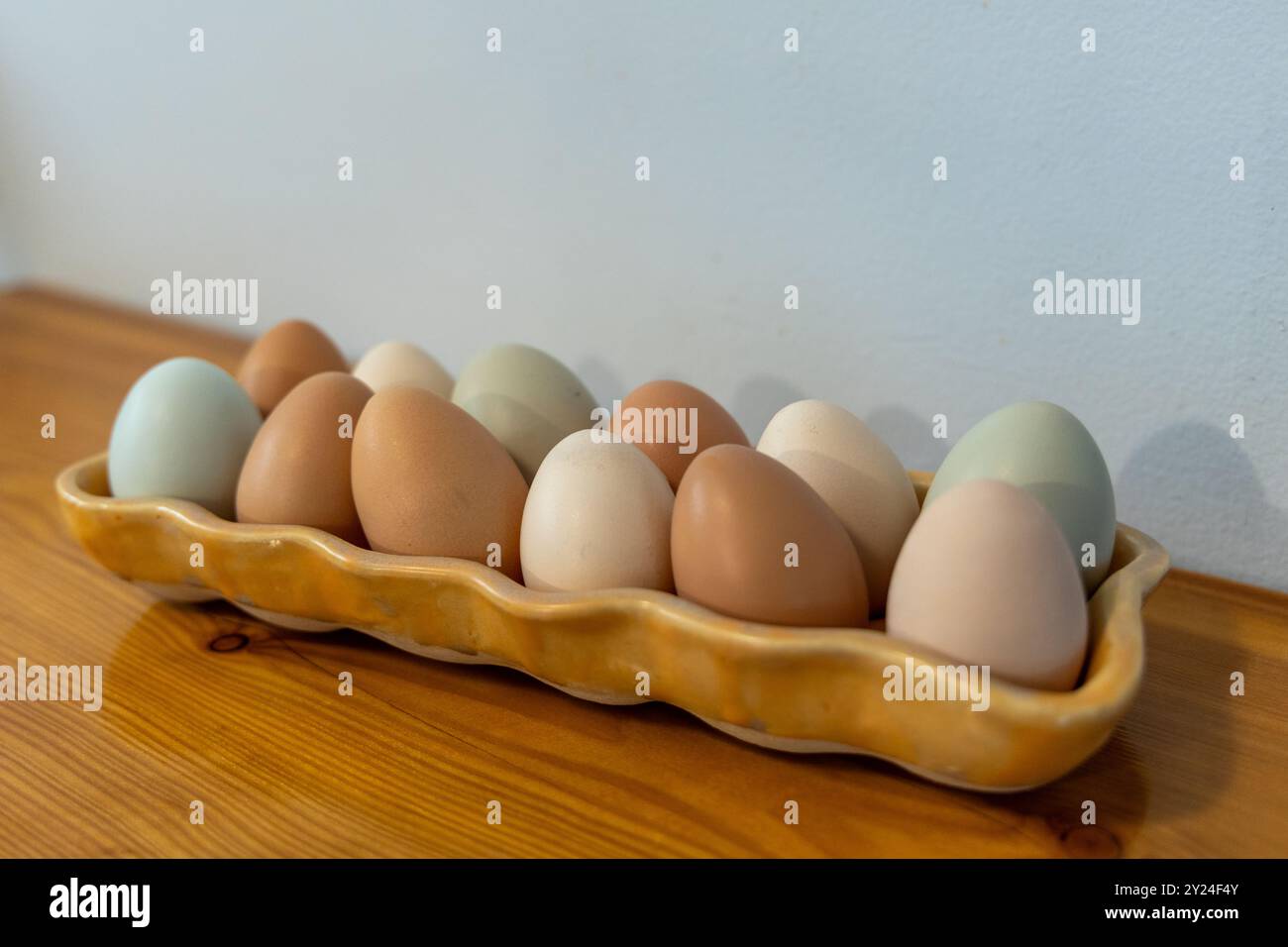 Multicolored eggs in a ceramic tray on a wooden surface Stock Photo
